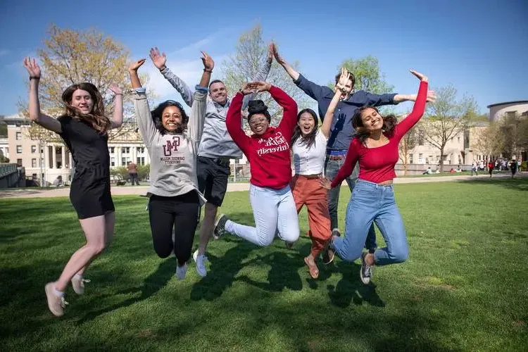 Students on the lawn jumping with hands in the air